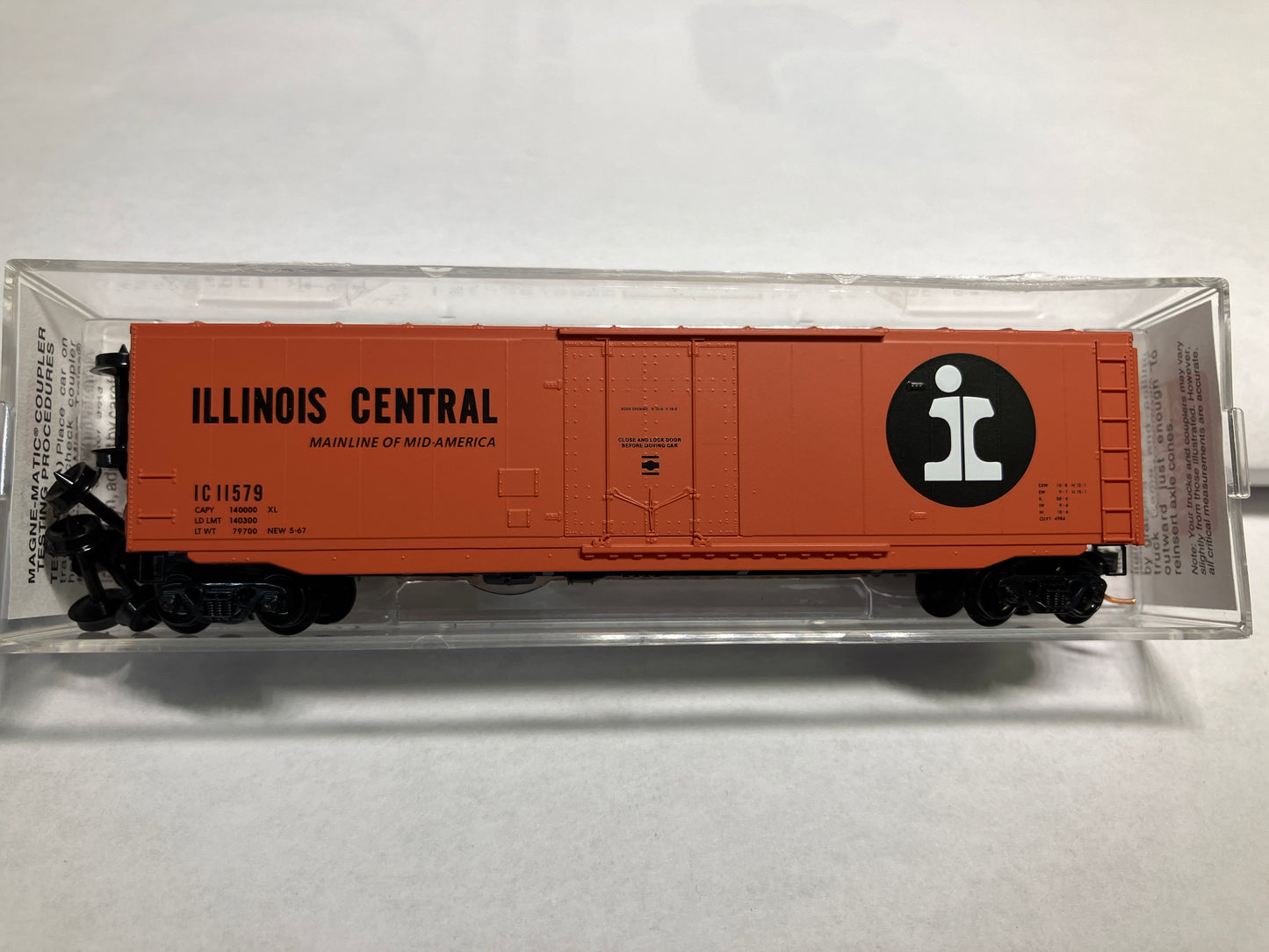 An orange Micro Trains model of an Illinois Central box car with a plug door, displayed in a clear plastic case.