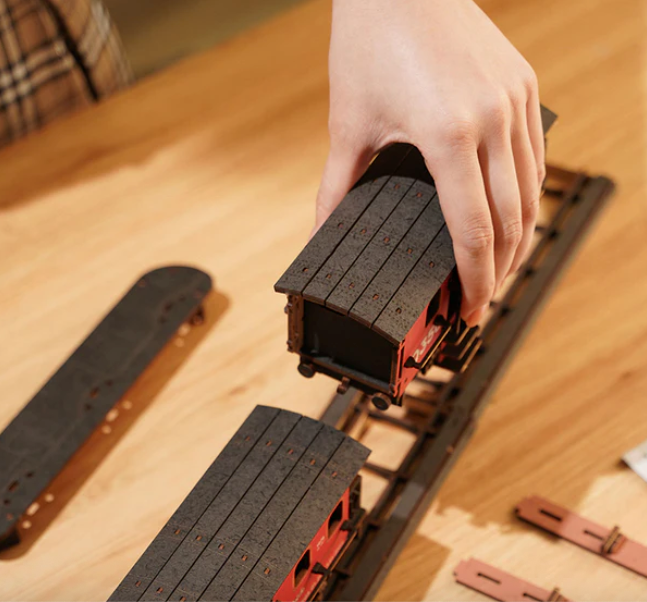 Hand placing a toy train on a track with wooden surface