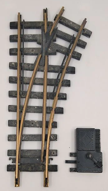 Brass manual switch track turnout with a four-foot diameter, two-foot radius, and molded plastic ties, mimicking a section of a toy train track.