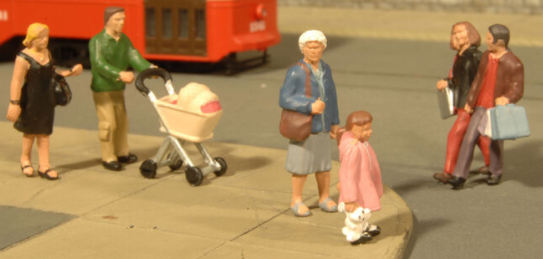 A set of three O scale strolling figures designed for model train setups, featuring a woman with a shopping bag, a girl in a pink coat, and an older woman with a walking stick.