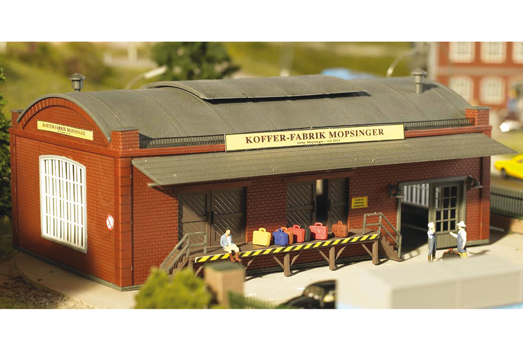 HO-scale model kit of a brown brick building with 'Köffers-Fabrik' signage, designed for model train setups.
