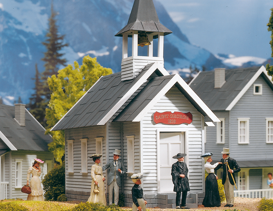 A model of a country church with figures in front and a steeple in the background, made from a plastic material, likely to be used for model train sets.