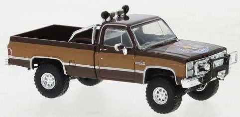A brown and dark brown die-cast model pickup truck with off-road tires, a front bumper guard, and roof-mounted lights, shown on a plain white background.