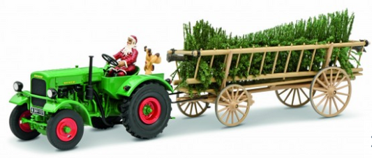 A diecast model of a green tractor with red wheels, towing a Christmas-themed trailer carrying a Christmas tree. The model features Santa Claus sitting on the tractor, and a small dog is also visible on the trailer.