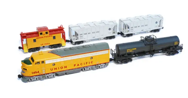 A set of four N scale model trains from Union Pacific, including a yellow caboose, two white boxcars, and a yellow and gray locomotive pulling a black tank car, displayed on a white background.