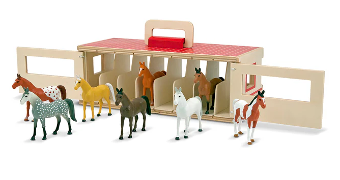 Set of toy horses in front of a wooden stable with a red top on a white background