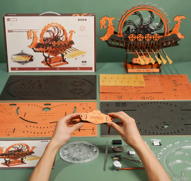 Mechanical model kit with hands assembling parts on a green table.
