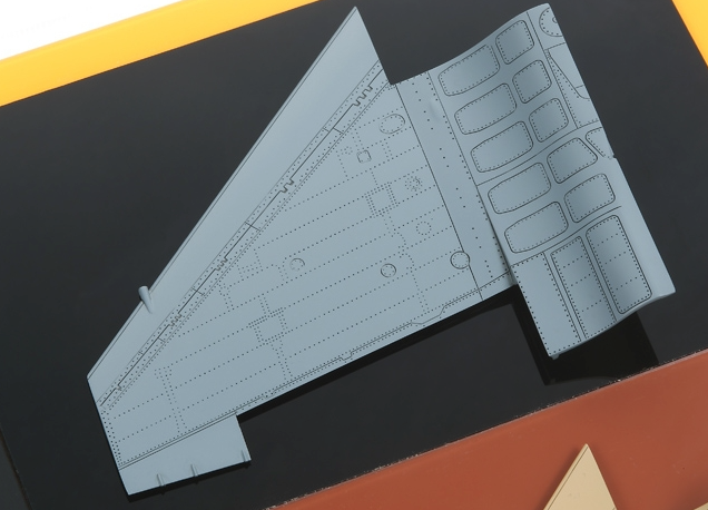 Gray model airplane wing on a black surface with yellow border