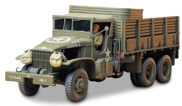 A detailed model of a vintage military truck in olive green with wooden cargo beds, shown on a clean white background with a soft shadow. A small figure of a driver is visible inside the cab.