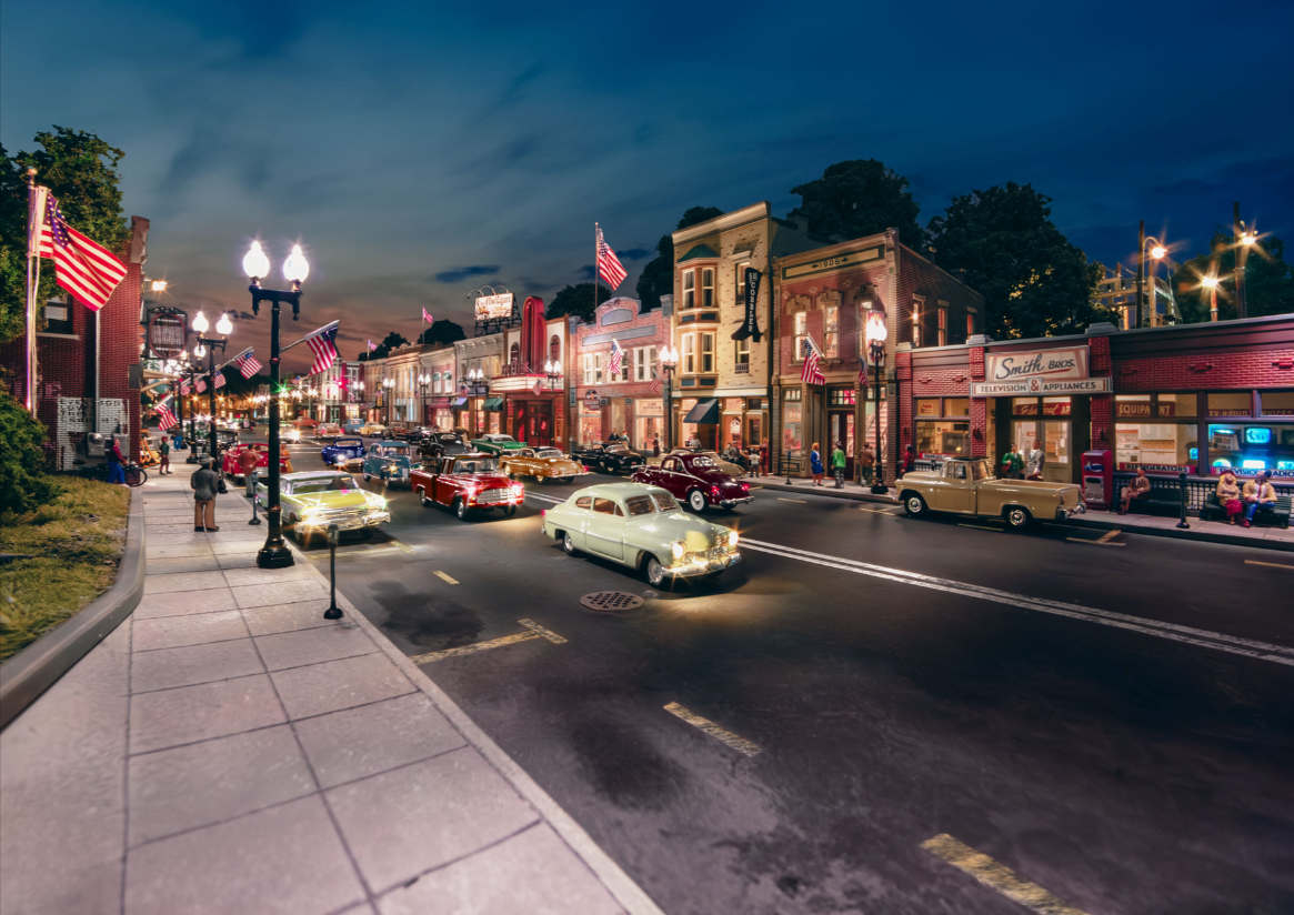 Downtown street scene with vintage cars and lit buildings at night.