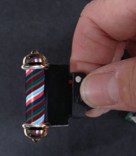 A close-up of a striped barber pole with animated ends, being manipulated by a human hand.