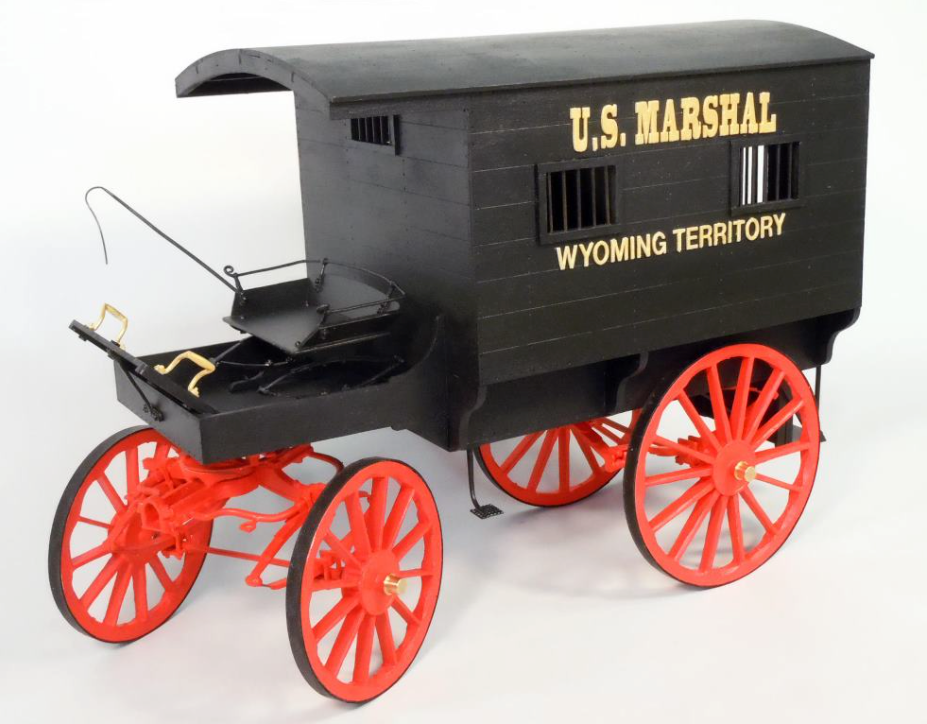 A model of a U.S. Marshal's jail wagon with a black body and red wheels and details, labeled 'Wyoming Territory'.