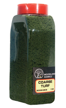 A shaker bottle filled with medium green coarse turf, labeled Woodland Scenics, for model train use.