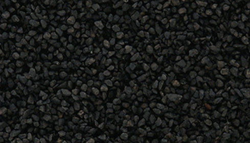 A close-up view of coarse ballast material for model train purposes, appearing as dark, round pebbles.