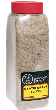 A container of Woodland Scenics FL631 Static Grass Flock in 'Wild Honey' color, used for model train setups.