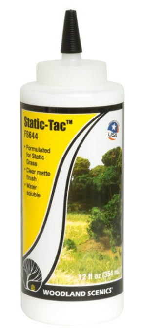 A bottle of Static-Tac adhesive for model train setups, with a clear label showing the product name and an image of grass.
