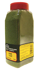 A bottle of Woodland Scenics Fine Turf Shaker in green color, used for model train setups.