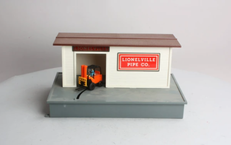 Lionel branded animated fork lift loader station for model railroads, featuring a small toy fork lift truck in front of a brown warehouse-style building with the text 'Lionville Pipe Co.'.